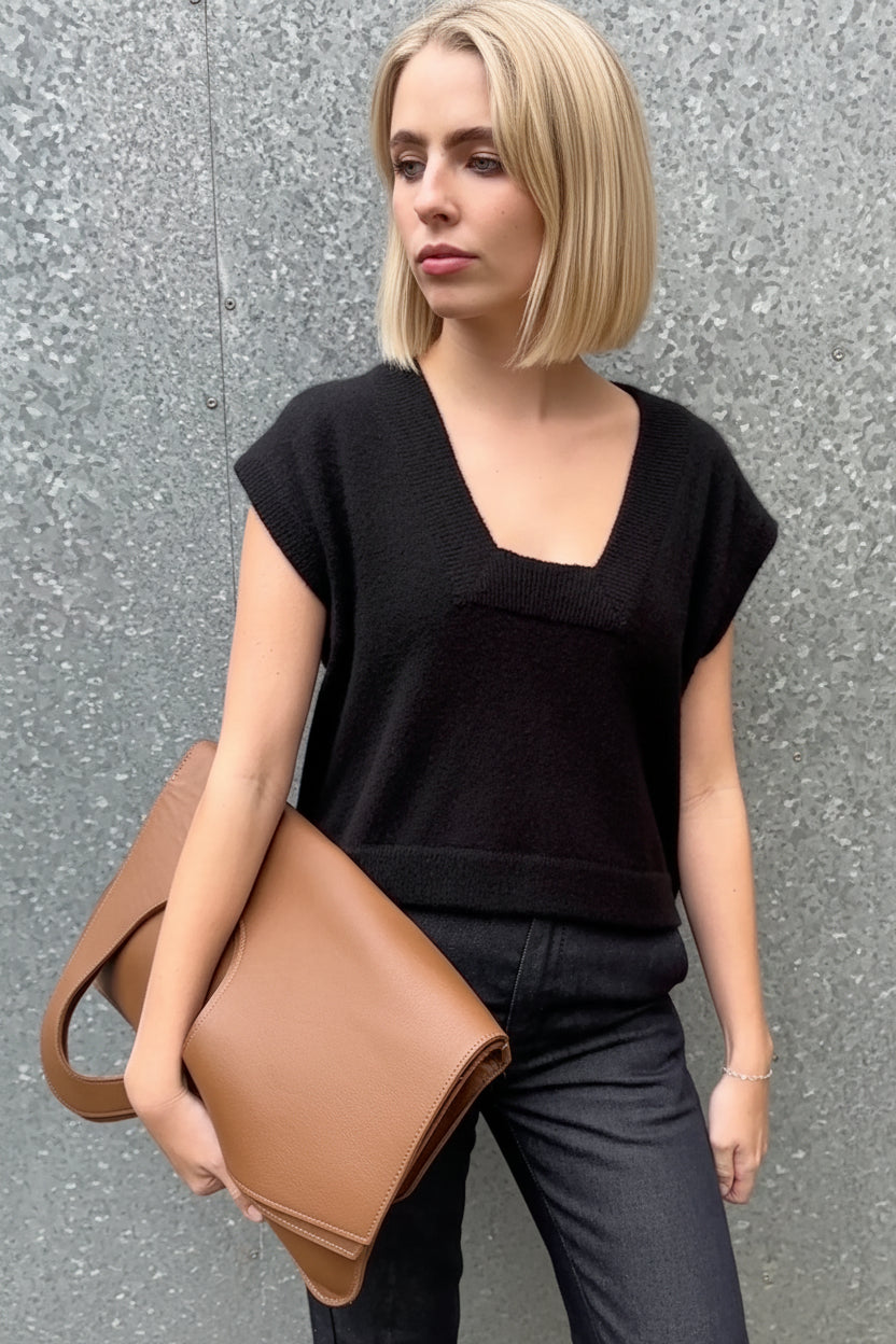 Woman wearing square neck cashmere silk inka tank top in black holding a brown leather bag against a gray wall