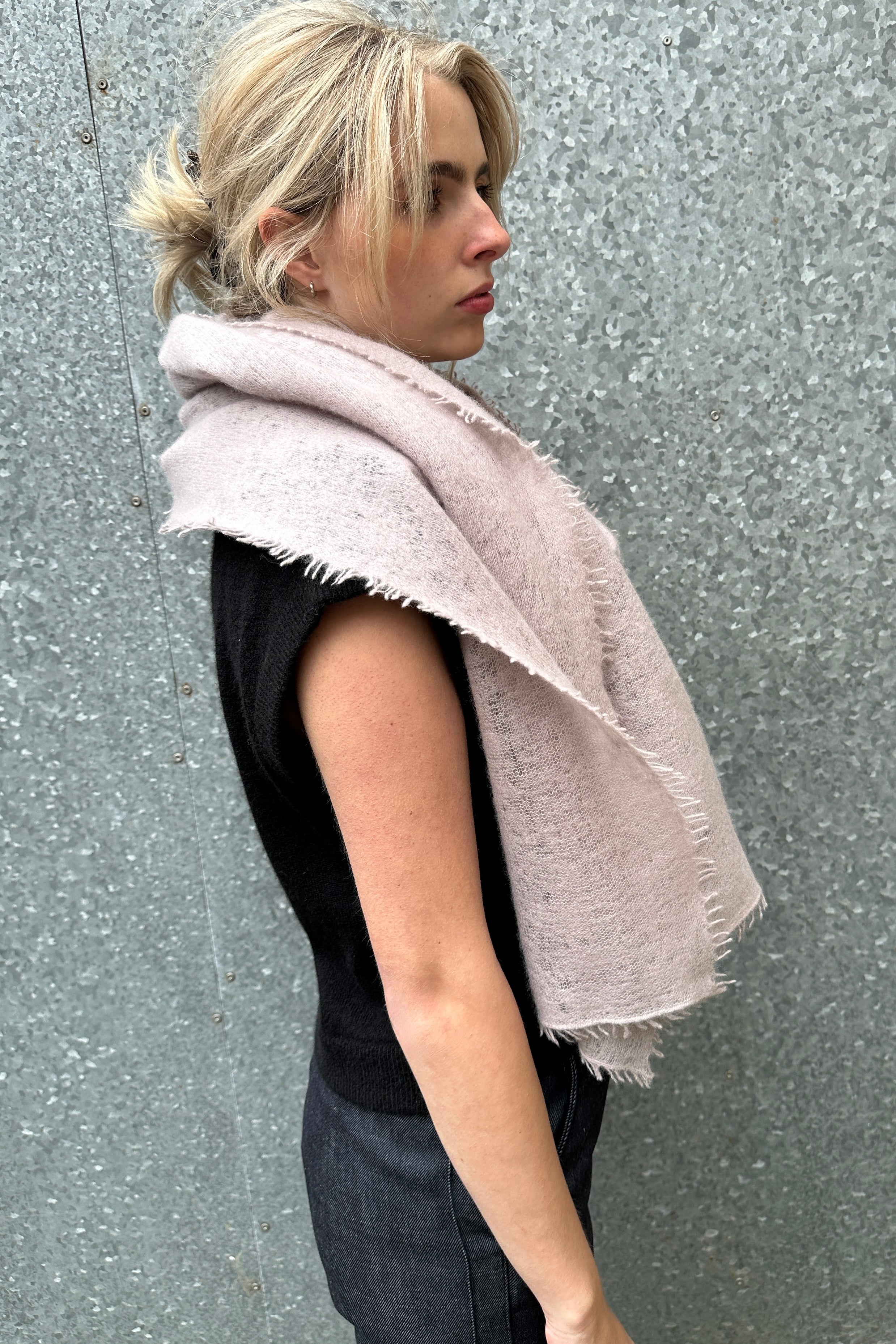 Woman wearing a light pink scarf against a gray wall