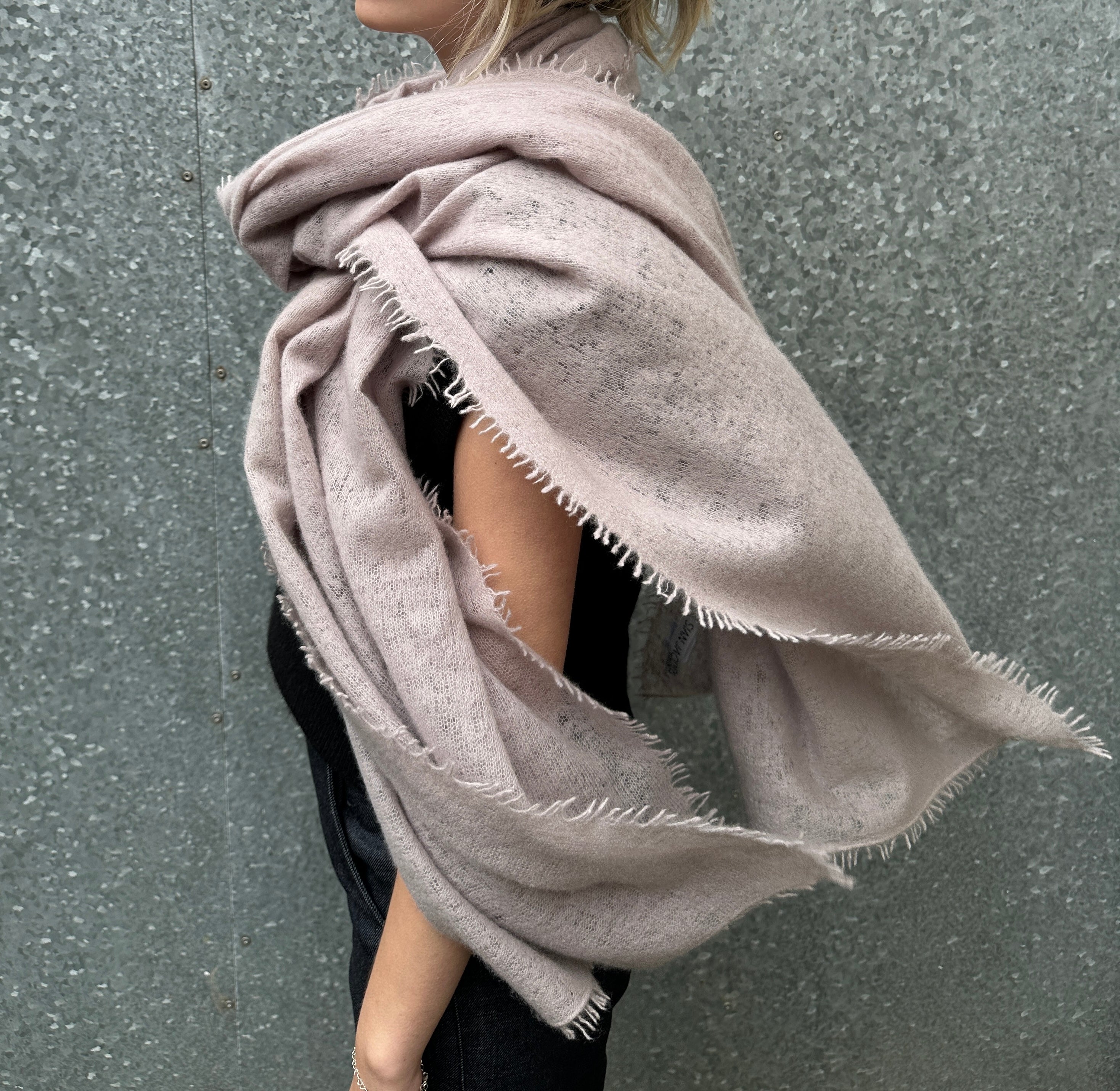 Person wearing a large beige scarf against a gray background