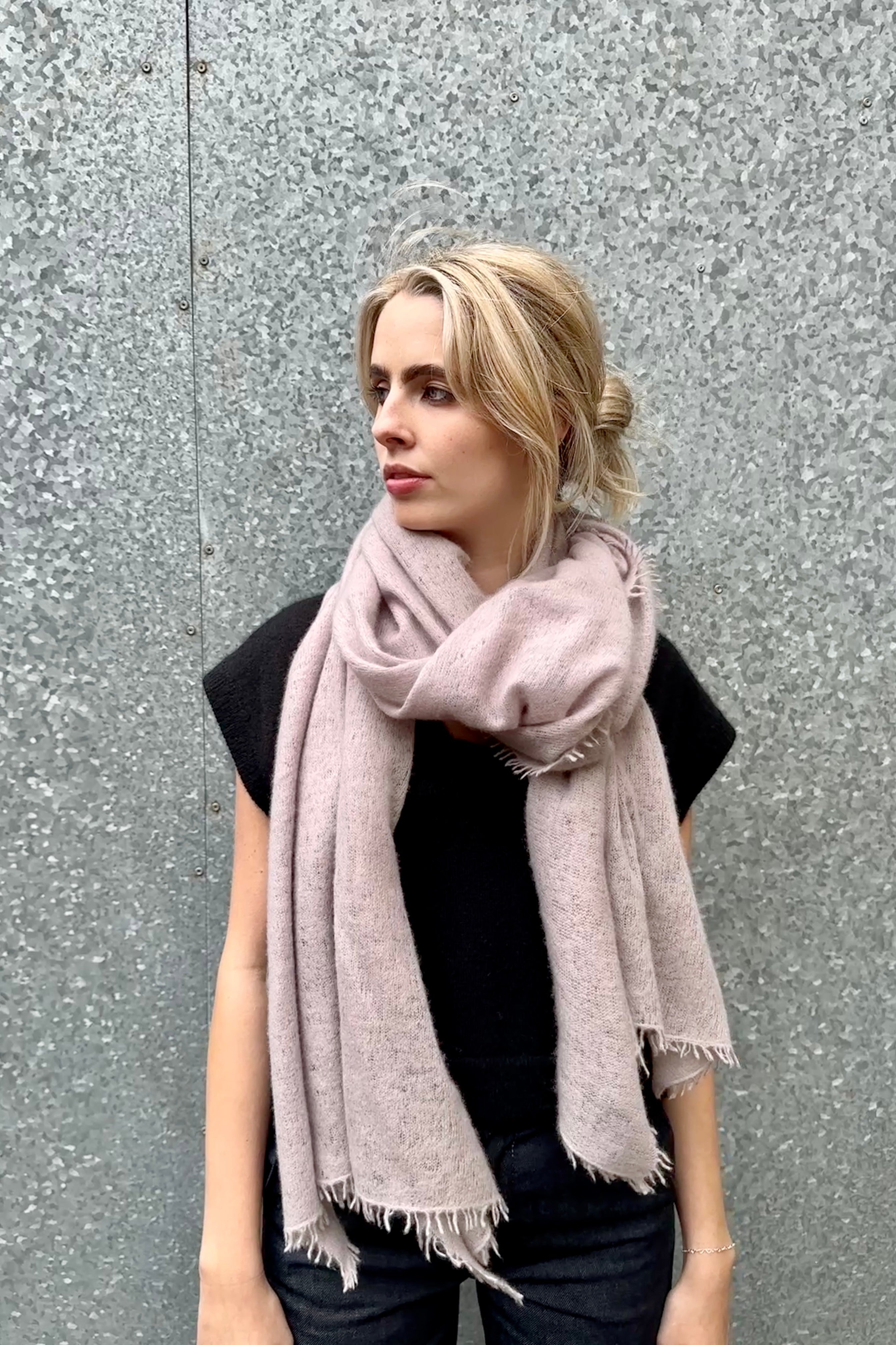 Woman wearing a light pink scarf against a gray wall