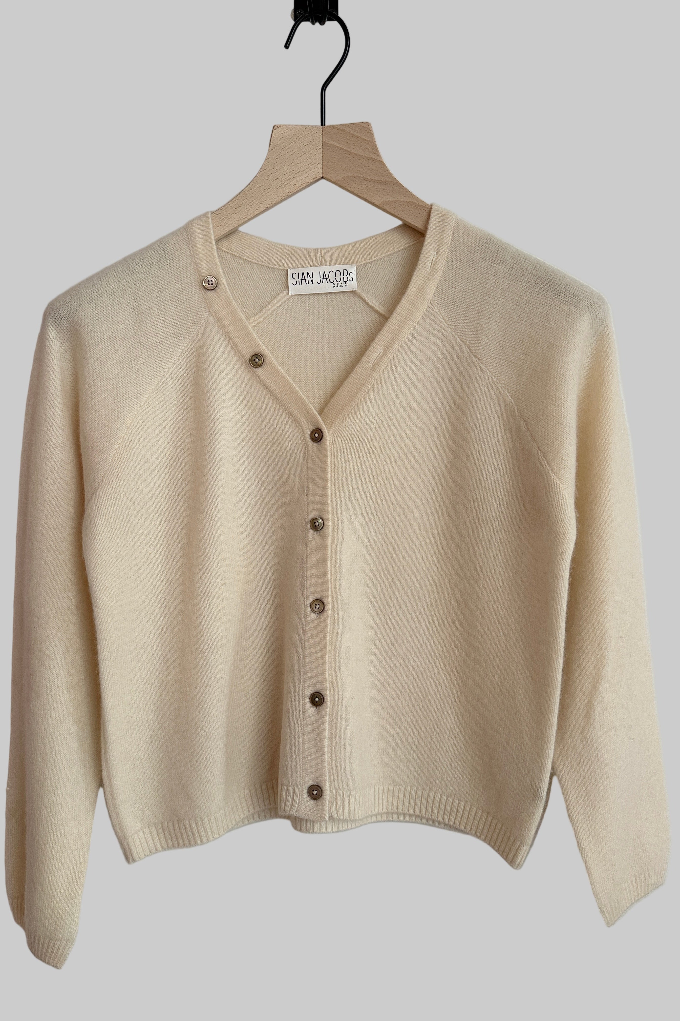 Zelia cream cashmere cardigan on a hanger against a white background