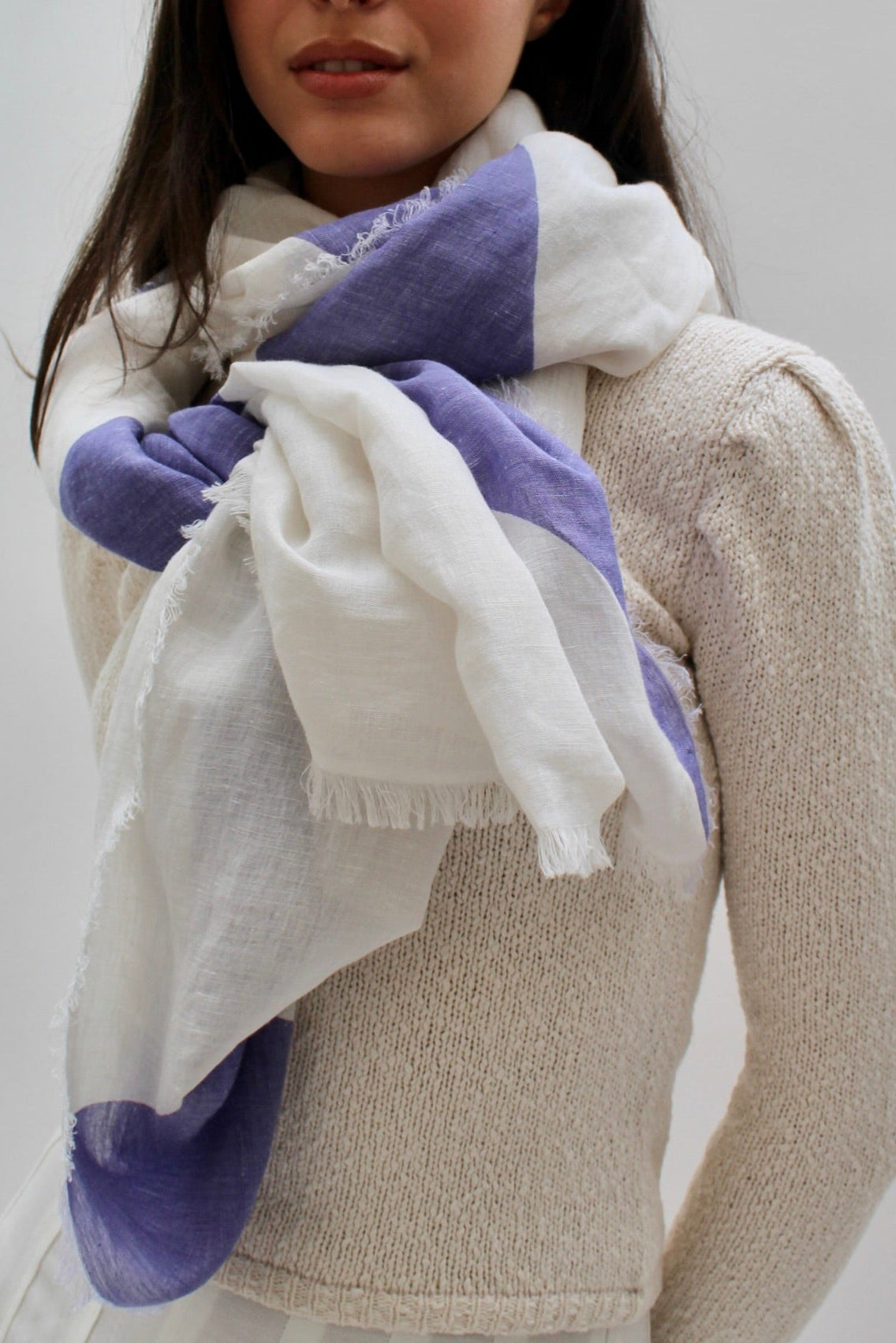 Person wearing a white and purple scarf with a neutral background