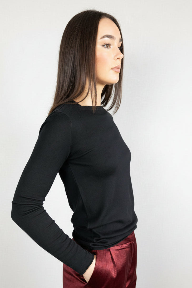 Woman wearing lassa  black long-sleeve top and burgundy pants against a neutral background