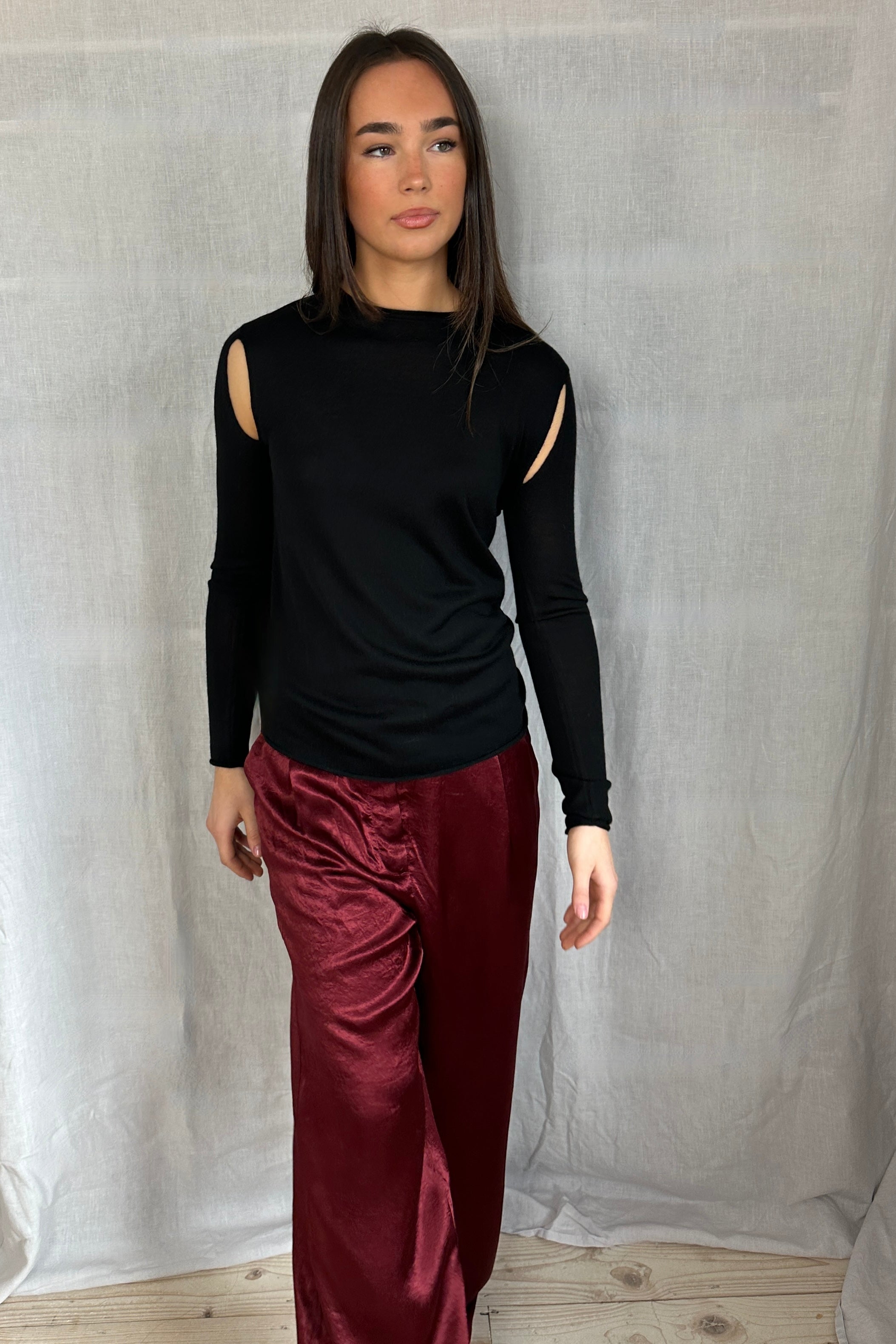 Model wearing a Richielu black long-sleeve top with cut-out design and red pants  walking