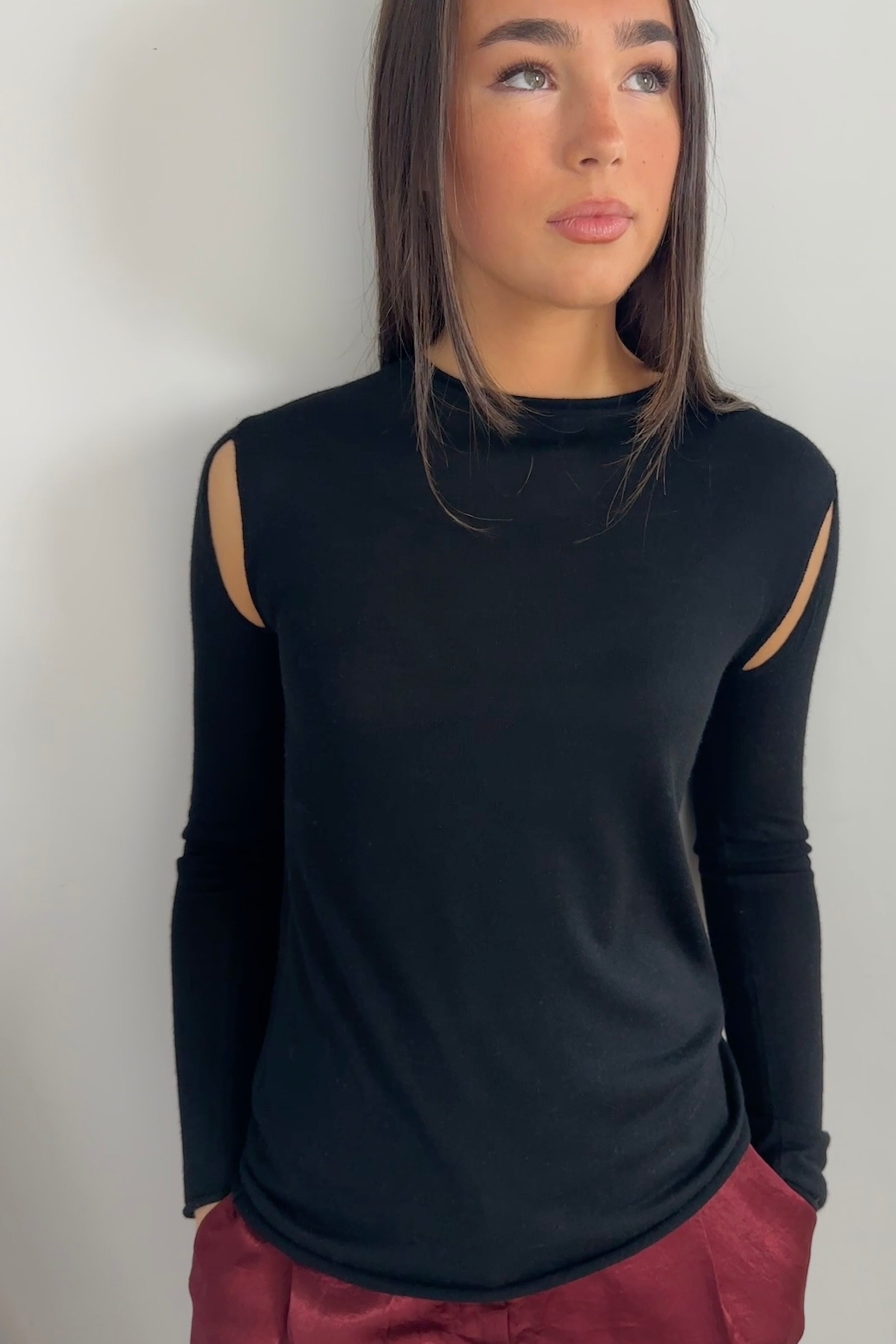 Model wearing a Richielu black long-sleeve top with cut-out design and red pants  close