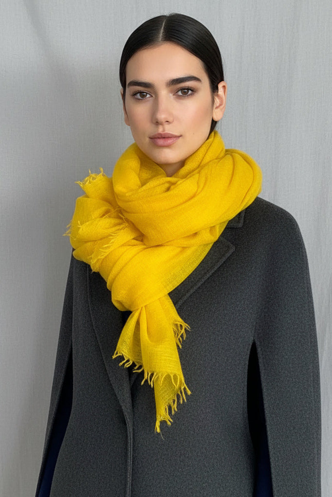 model wearing a bright mustard yellow scarf over a dark blue sweater against a neutral background