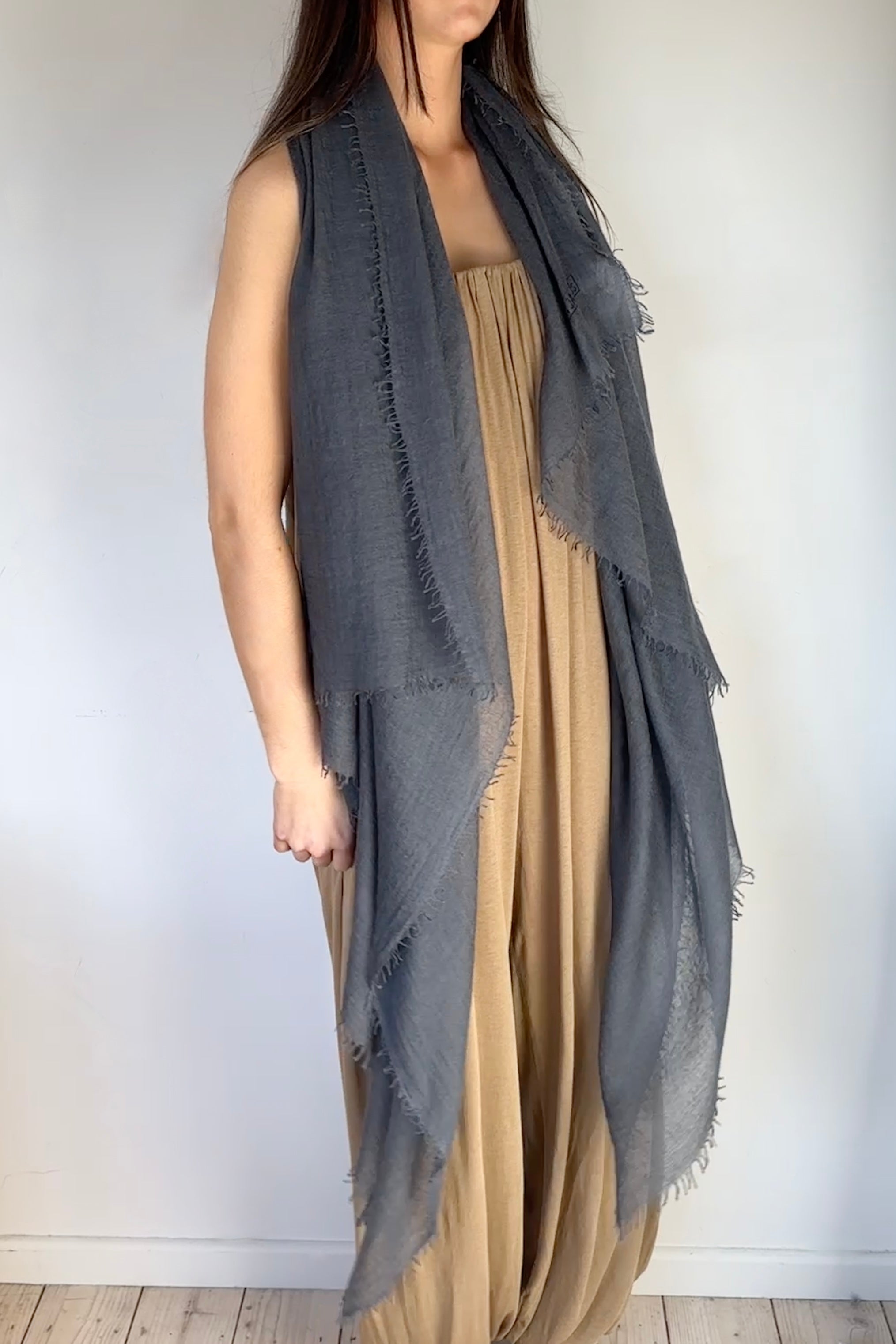 model wearing a long, dark gray cashmere marmee petrol scarf over a beige dress against a white background