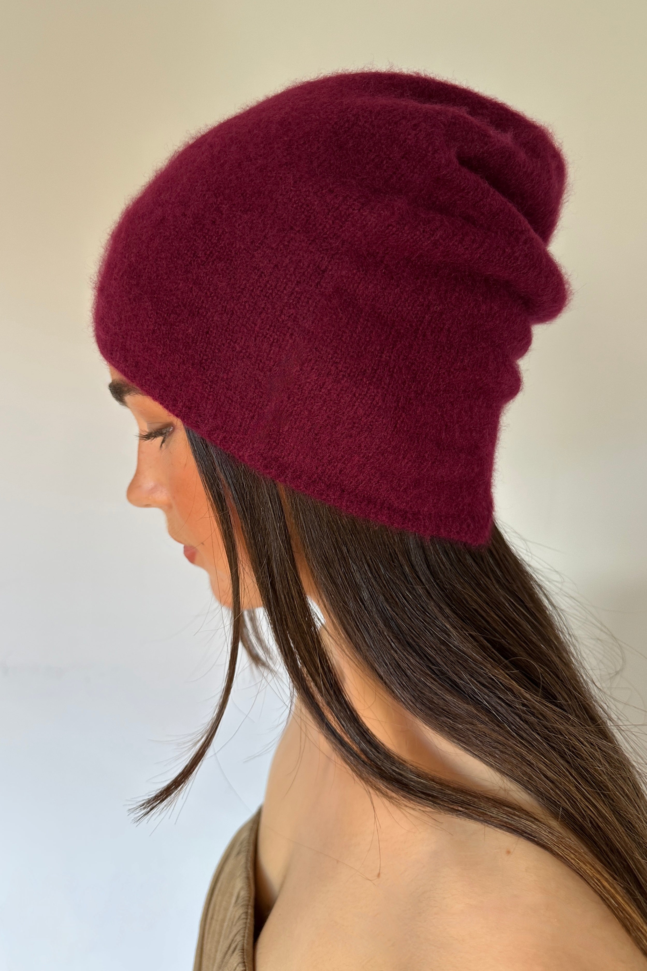 Maroon knit beanie worn by a person with a neutral background burgundy wine