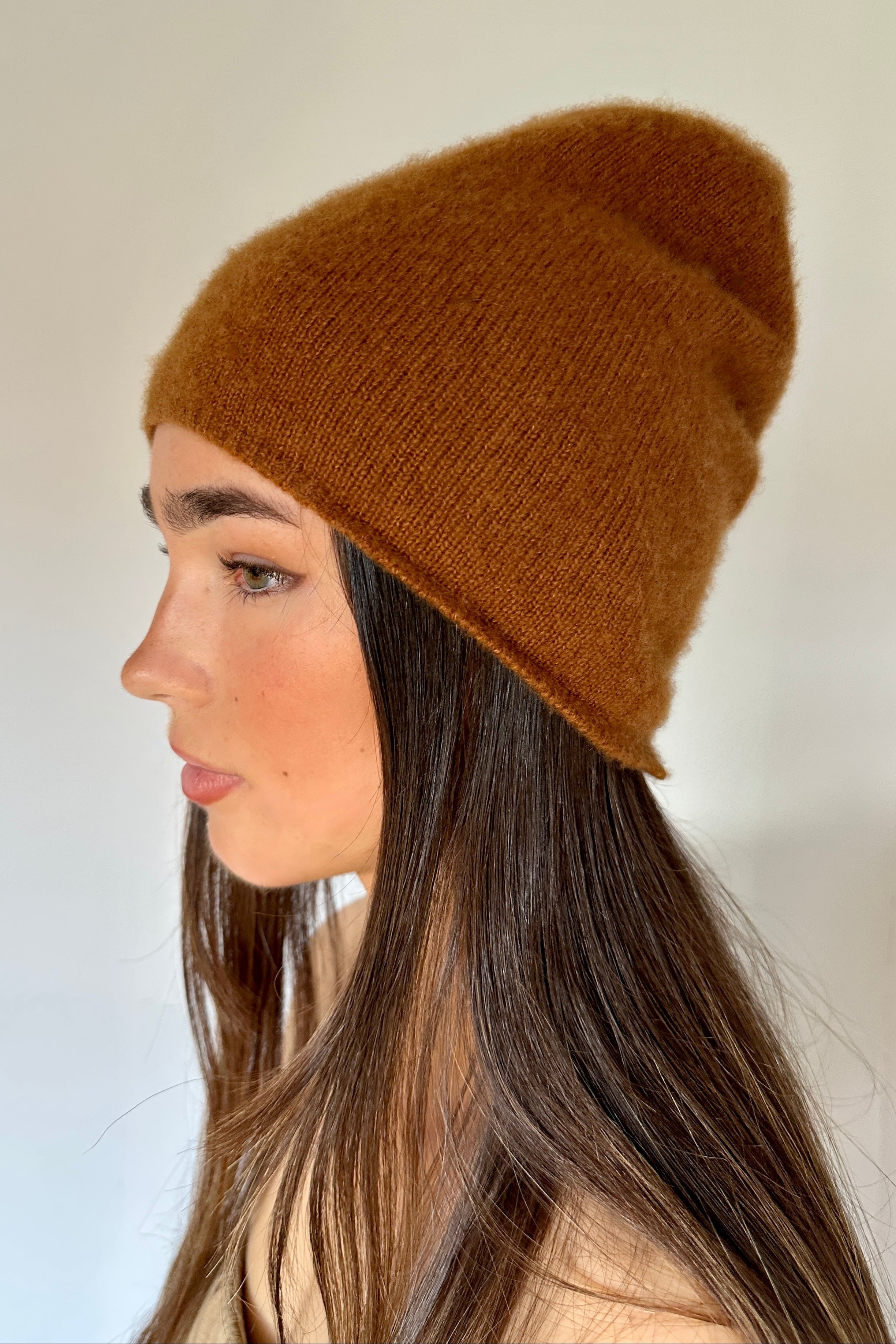 Woman wearing a  beety brown knit cashmere silkl beanie against a plain background
