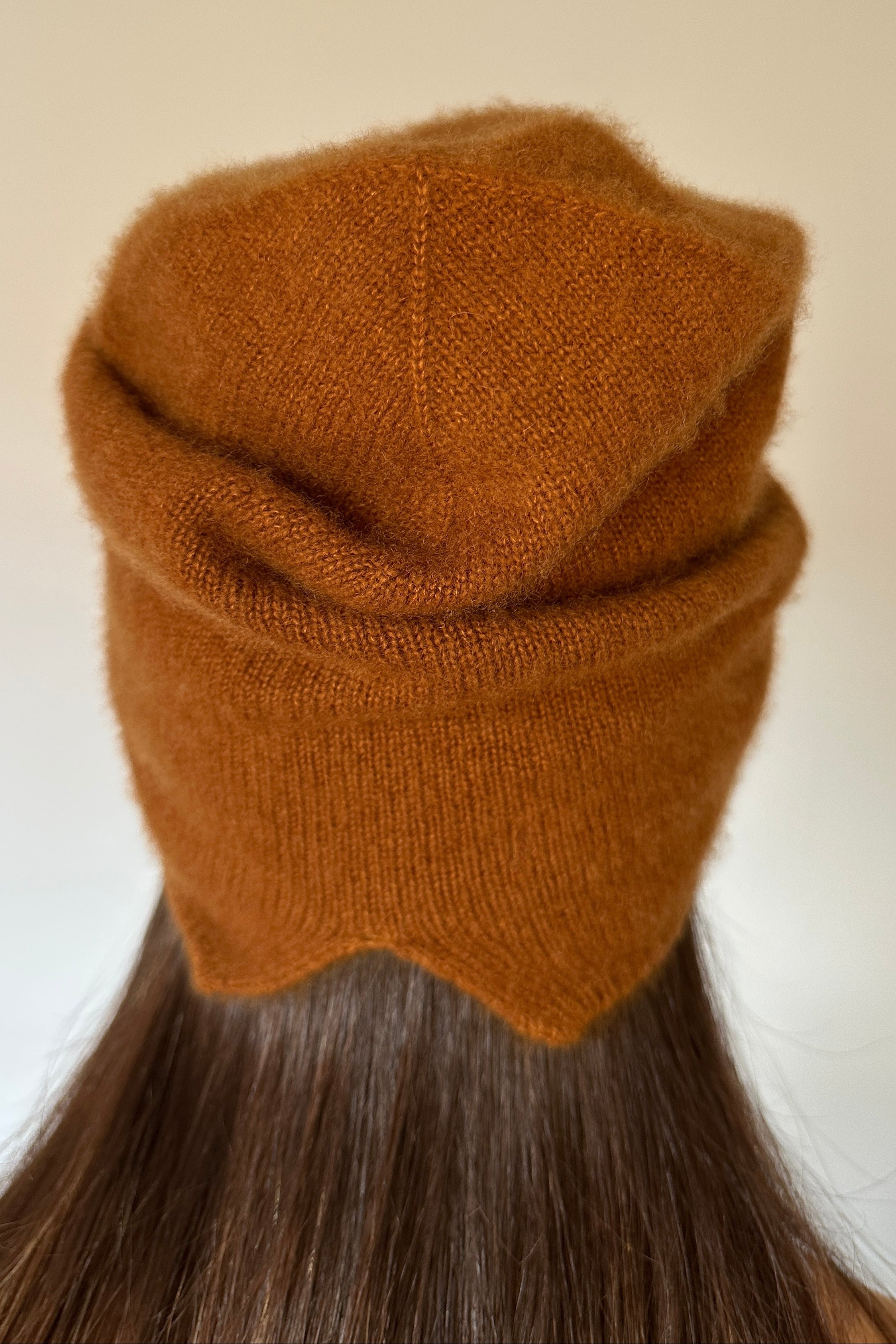 Woman wearing a  beety brown knit cashmere silkl beanie against a plain background back view