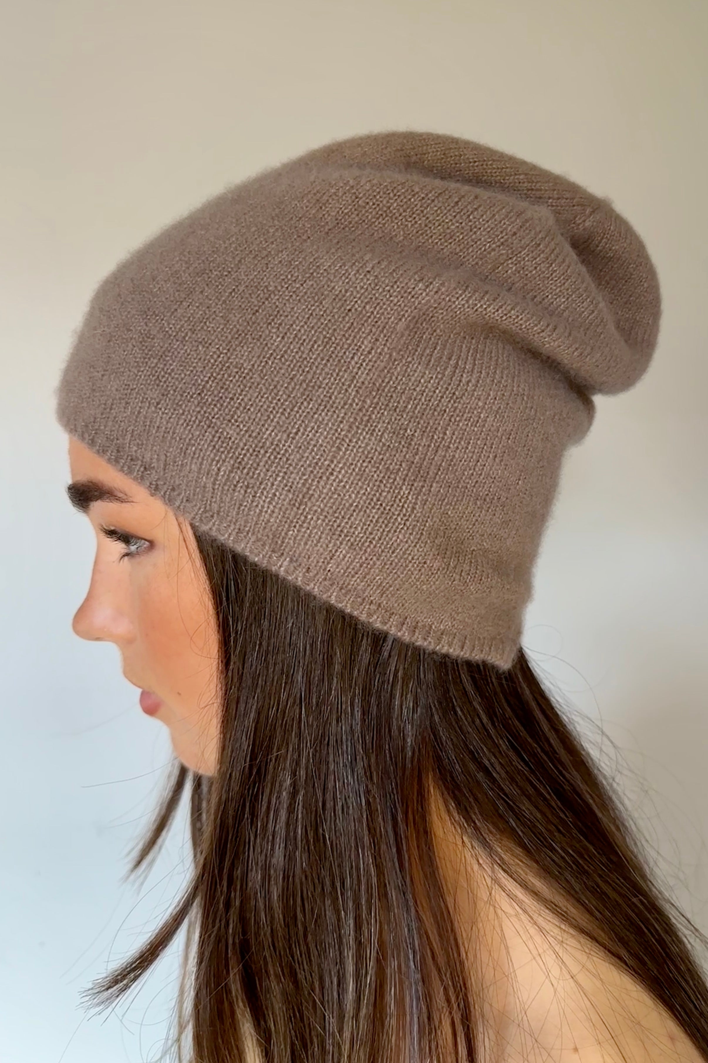 Woman wearing a  beety brown knit cashmere silkl beanie against a plain background side view