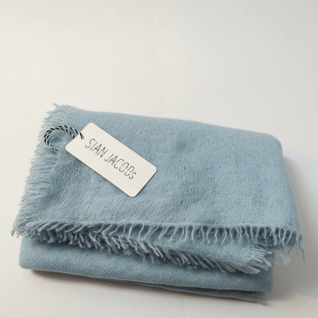 Light blue blanket with a 'Sian Jacobs'  tag on a white surface