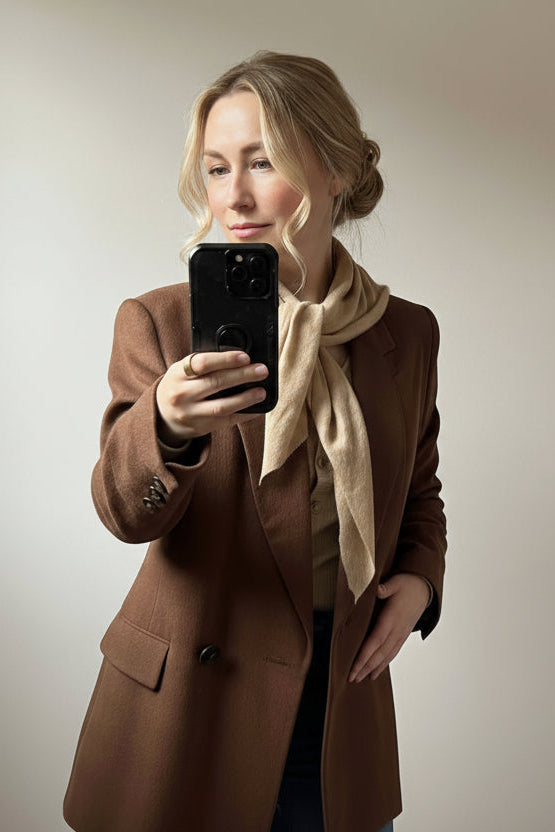 Person taking a mirror selfie wearing a brown coat indoors.