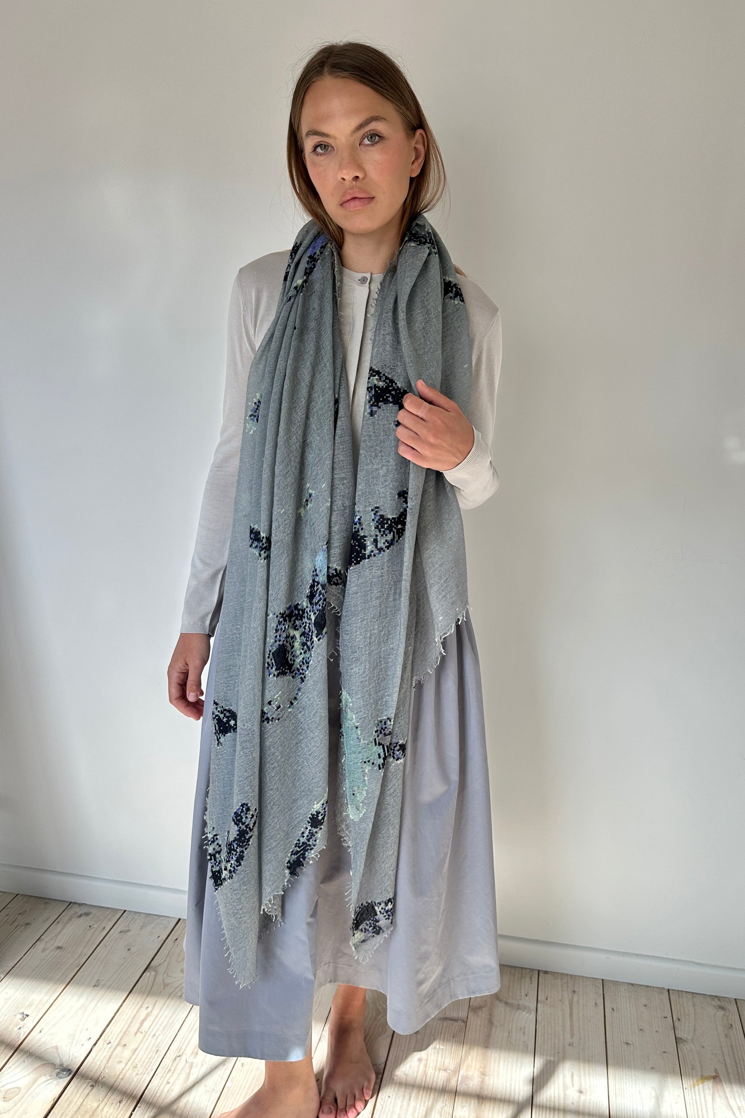 Woman wearing a light gray scarf with black floral pattern in a minimal indoor setting.