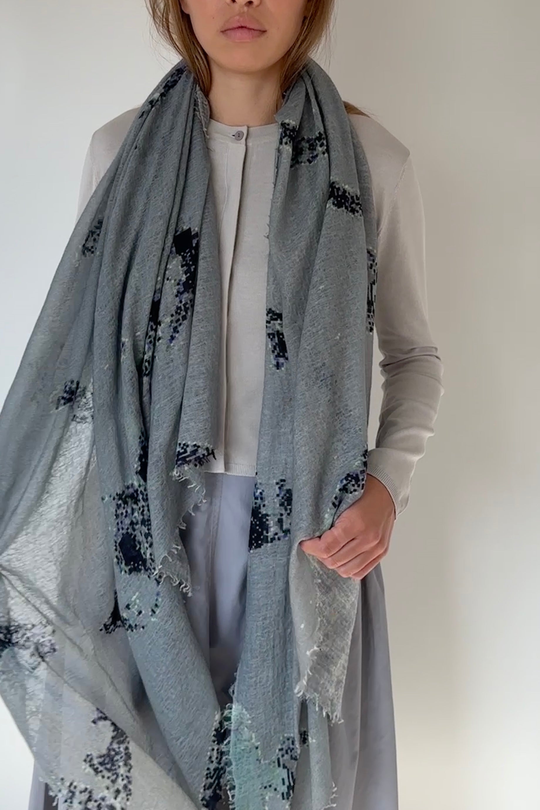 Person wearing a light gray scarf with black floral patterns on a plain background