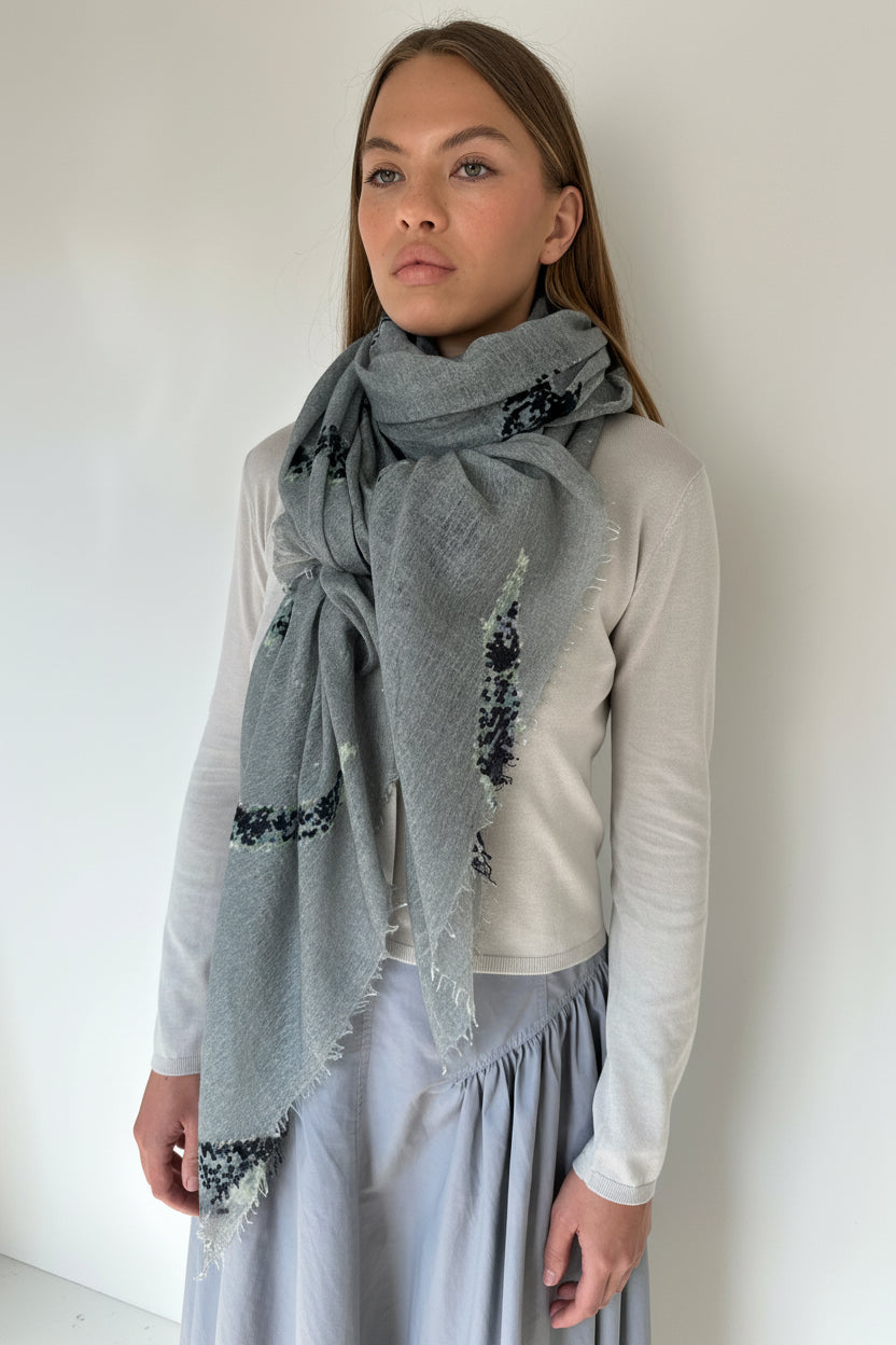 Woman wearing a gray scarf with black floral patterns on a plain background