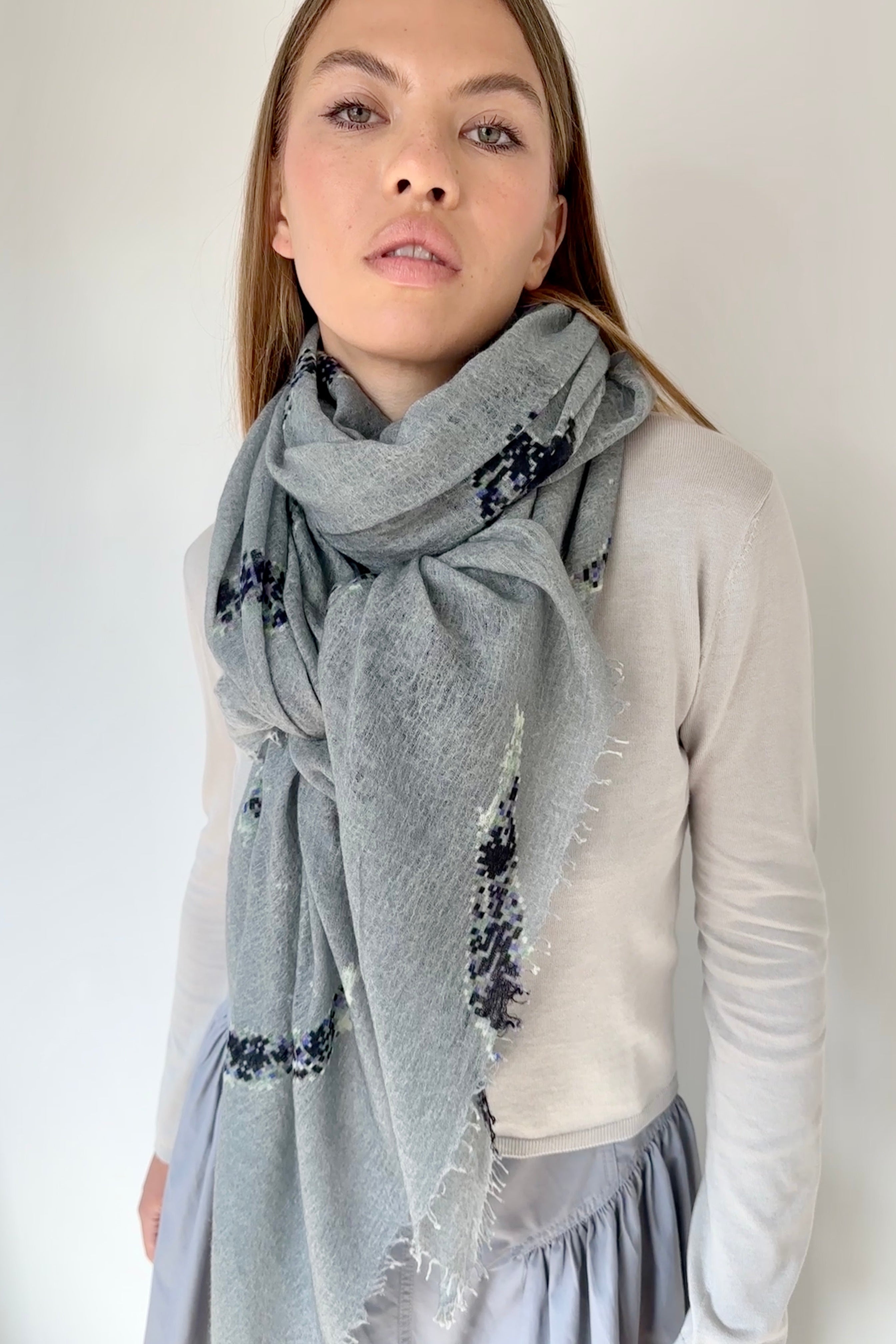 Woman wearing a gray scarf with floral embroidery on a plain background