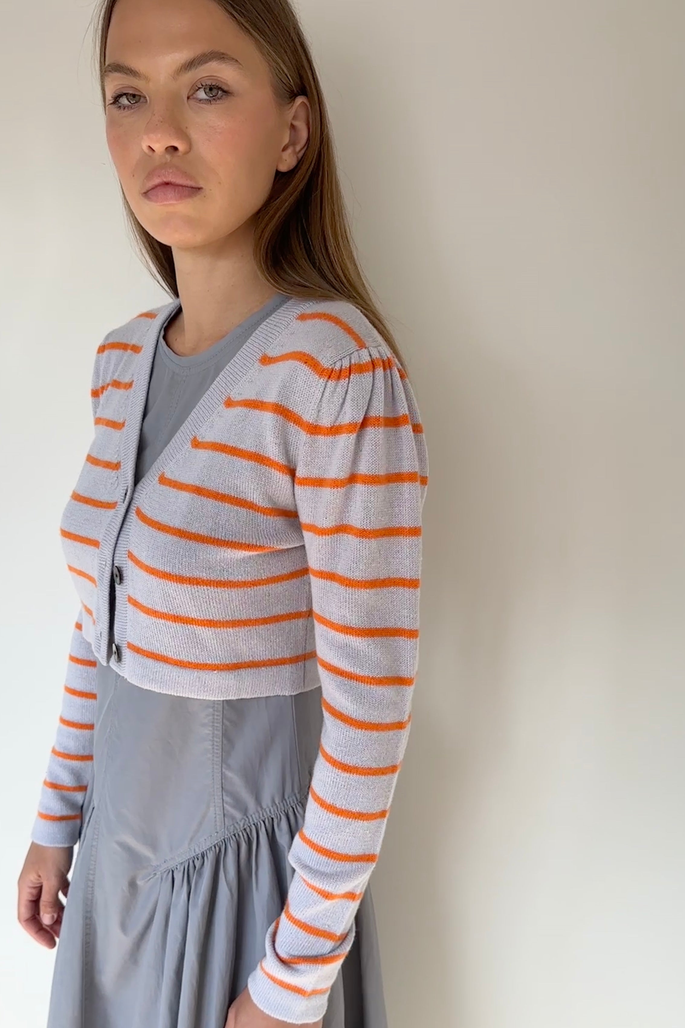 Woman wearing a gray and orange striped cardigan over a gray dress against a plain background