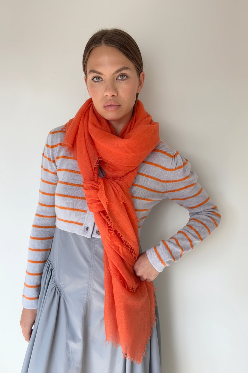 Woman wearing a striped sweater and orange scarf against a plain background