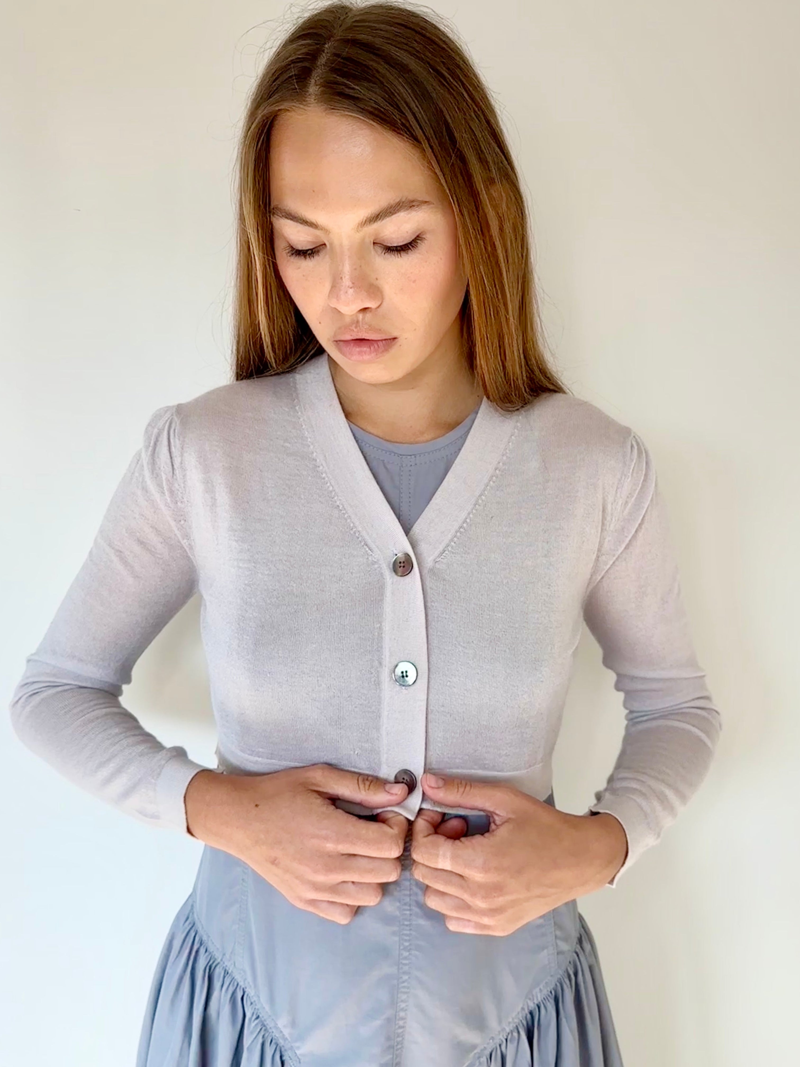 Woman wearing a light gray cardigan over a blue dress against a plain background
