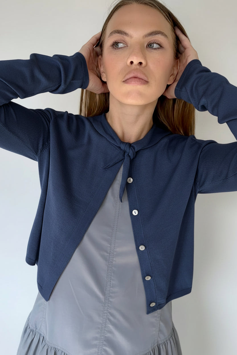 Woman wearing a navy cardigan over a grey dress against a plain background