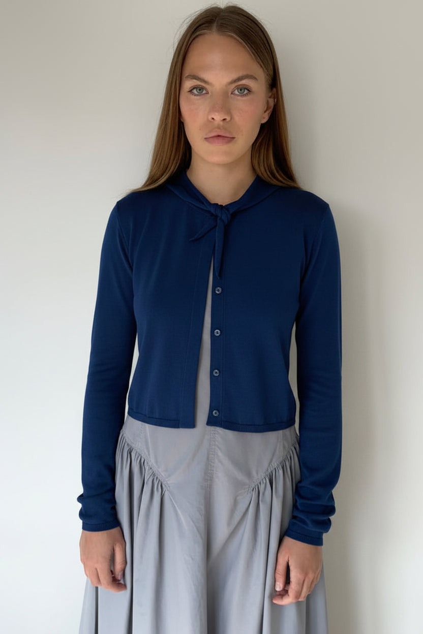 Woman wearing a navy cardigan over a light blue dress against a white background