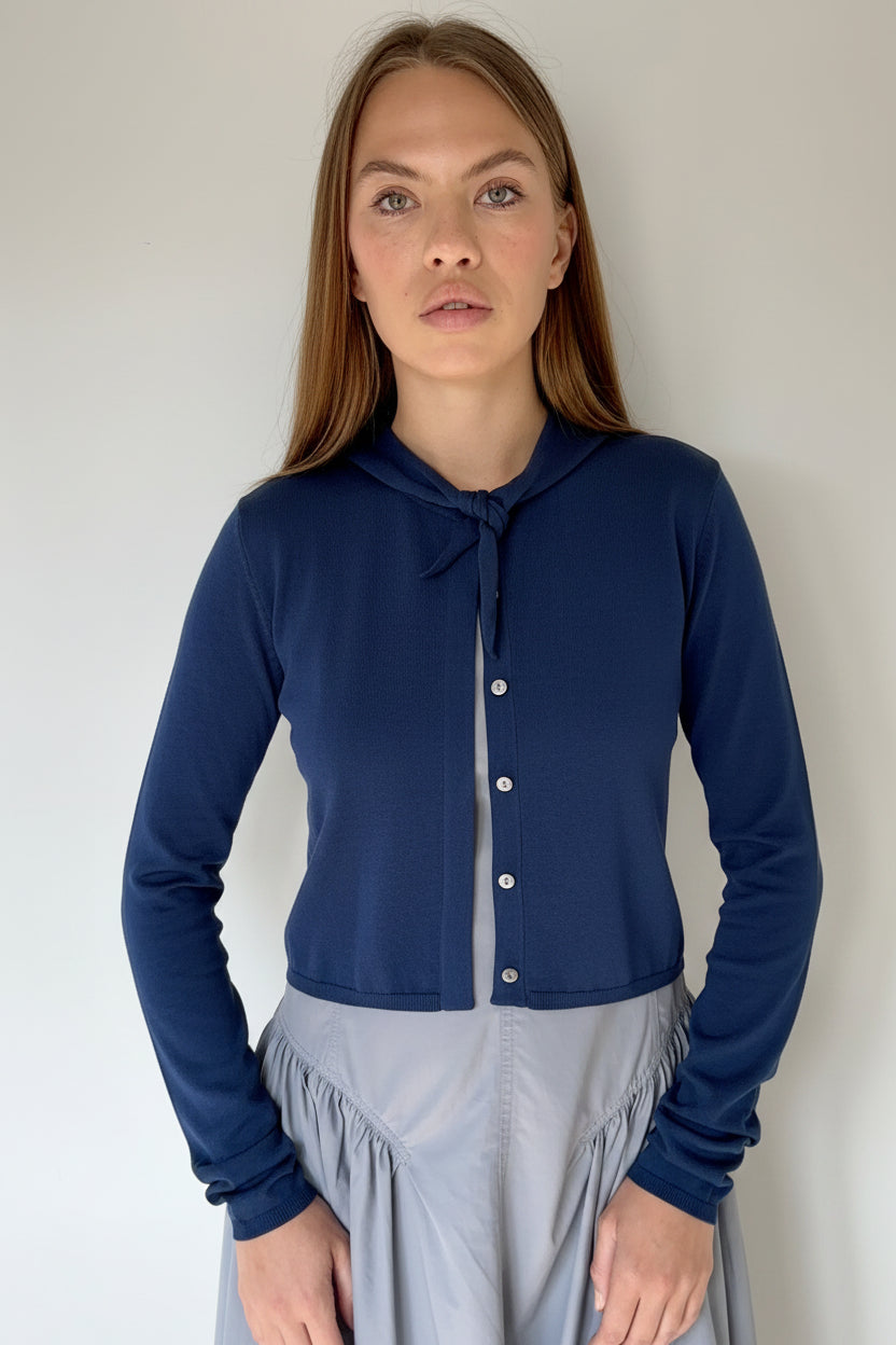 Woman wearing a navy cardigan over a blue dress against a plain background