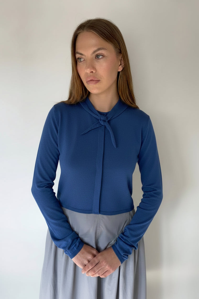 Woman wearing a navy blue cardigan  standing against a plain background.