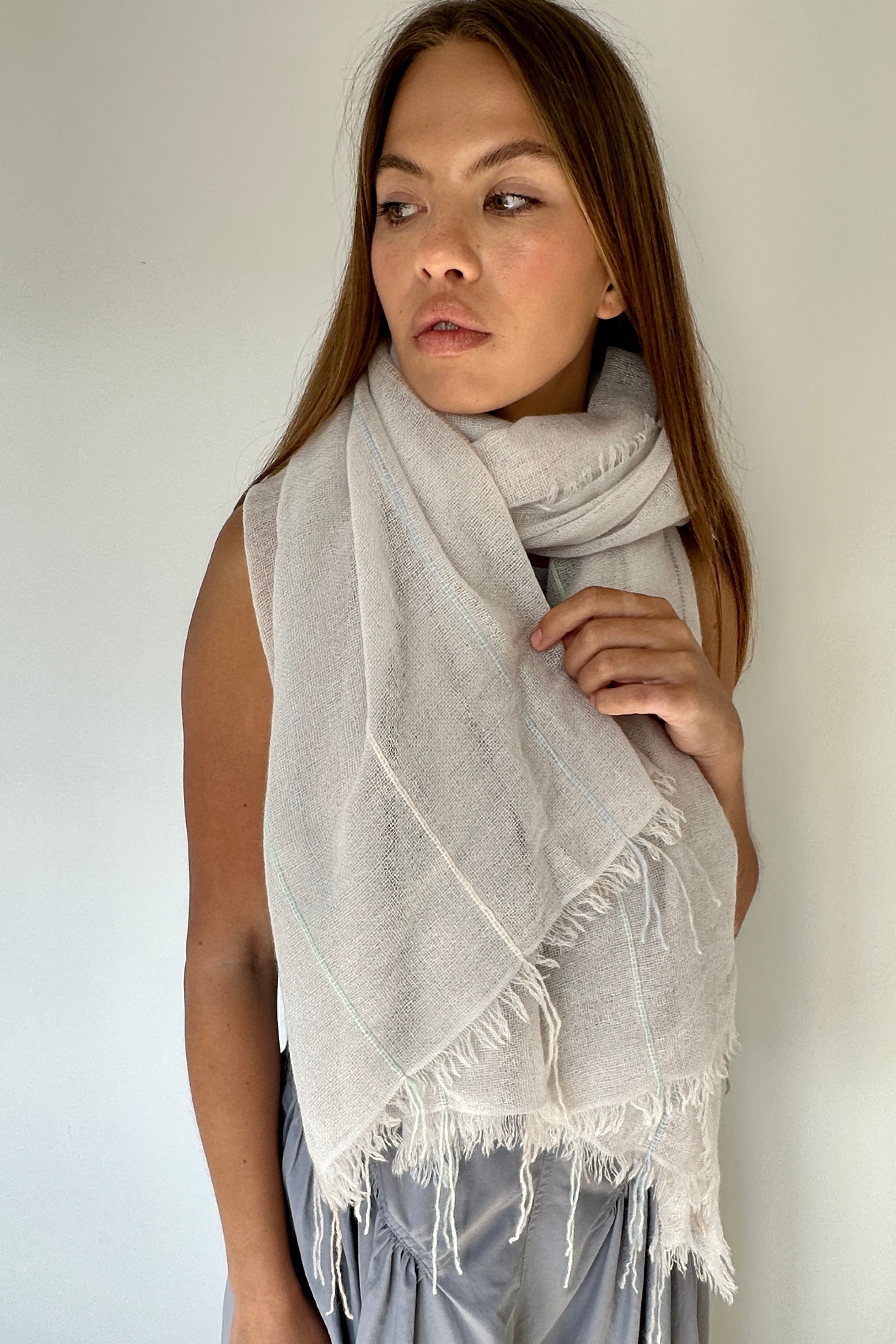 Woman wearing a light gray scarf with fringes against a plain background