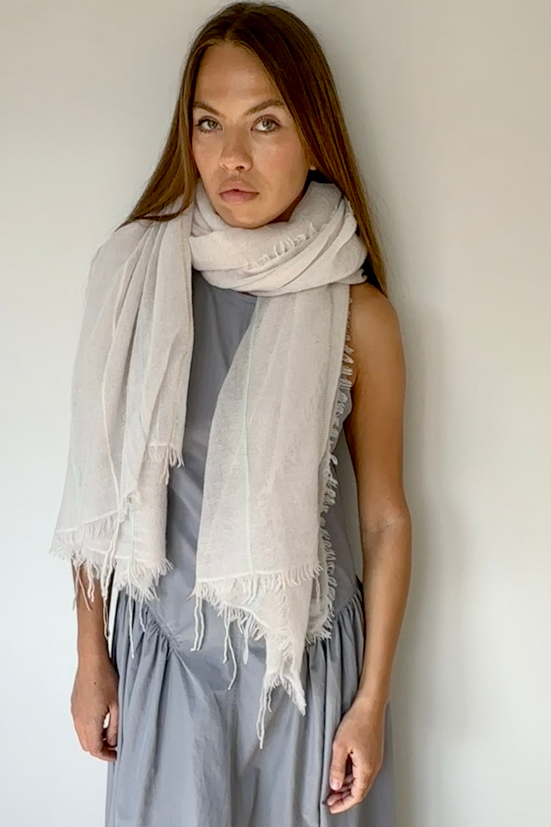 Woman wearing a light gray scarf and dress against a plain background