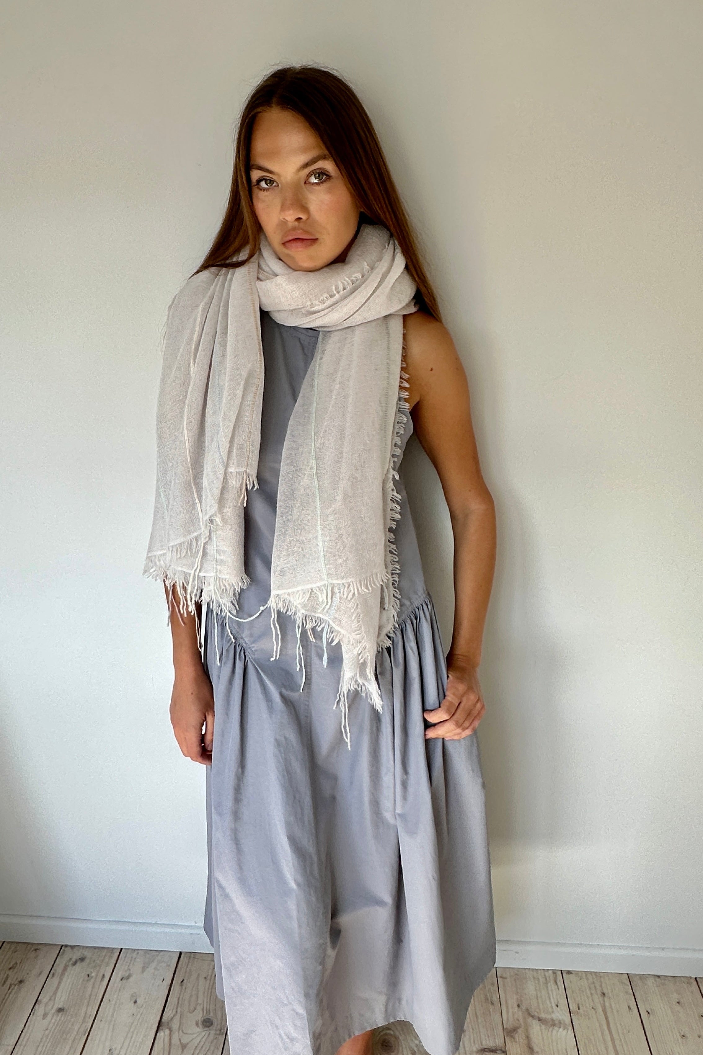 Woman wearing a light gray dress and scarf against a plain wall.