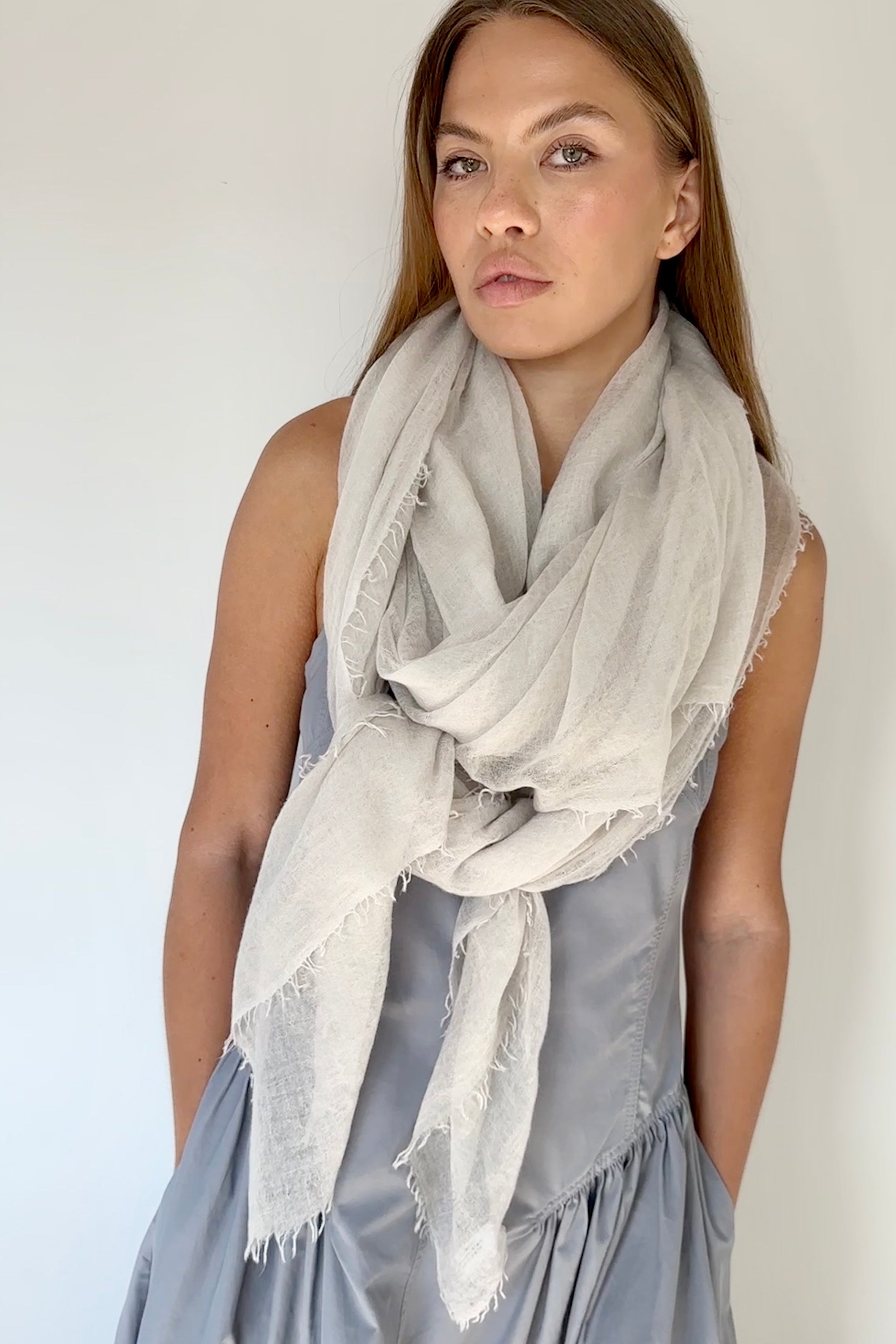 Woman wearing a light gray scarf and a gray dress against a white background