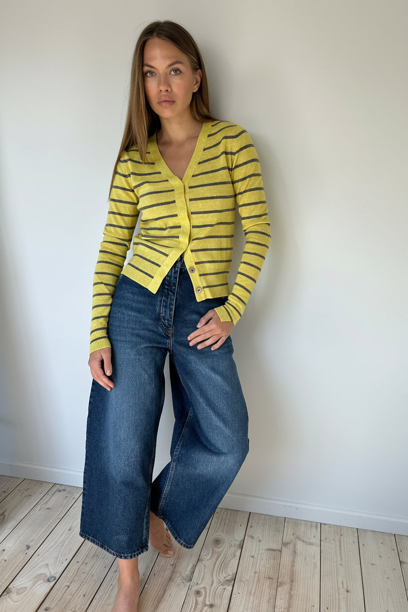 Woman wearing a yellow striped cardigan and blue jeans against a white wall.