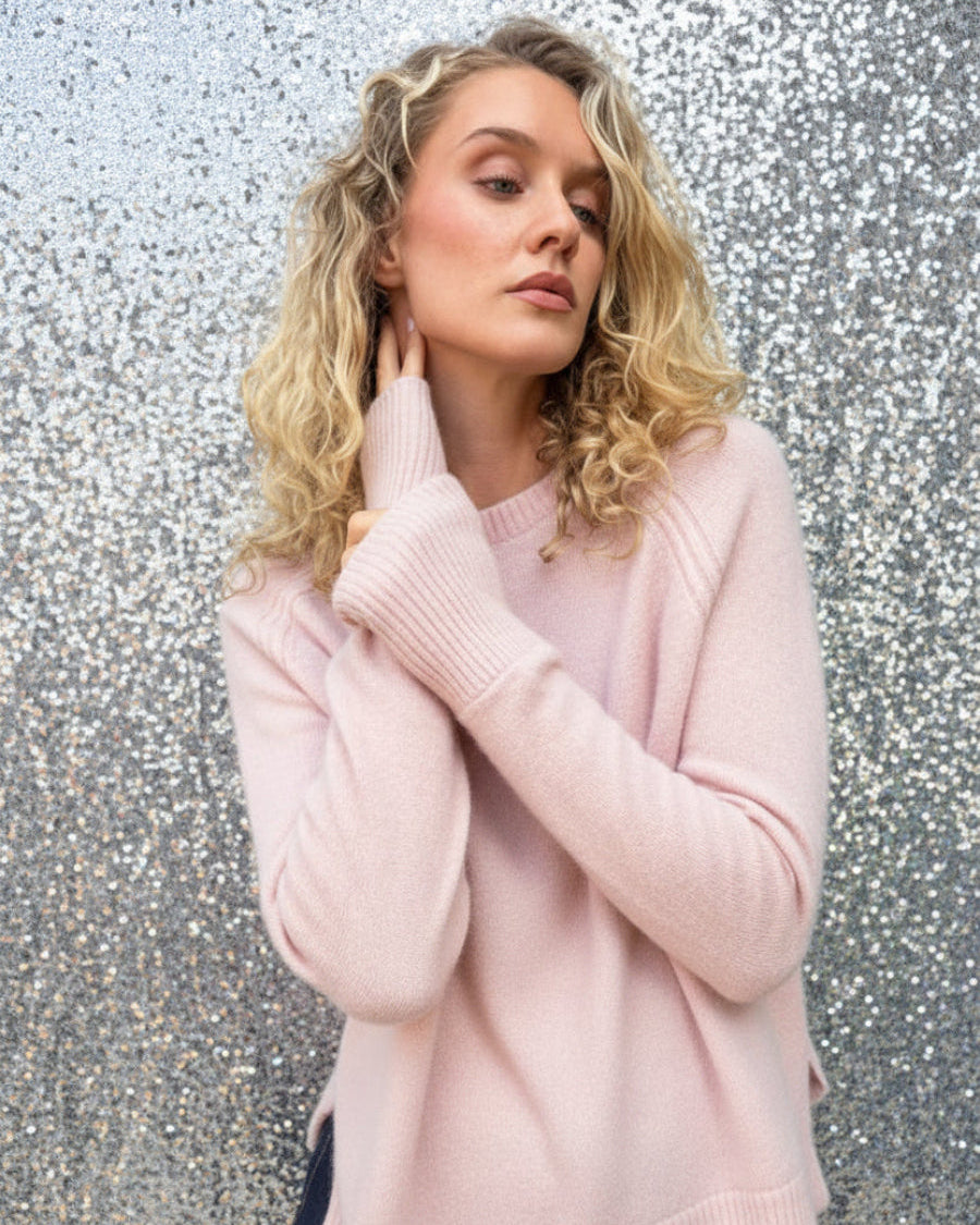 model in pale pink sweater against a silver wall